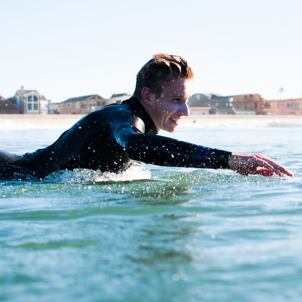 Person in a wetsuit paddling in the water with houses in the background