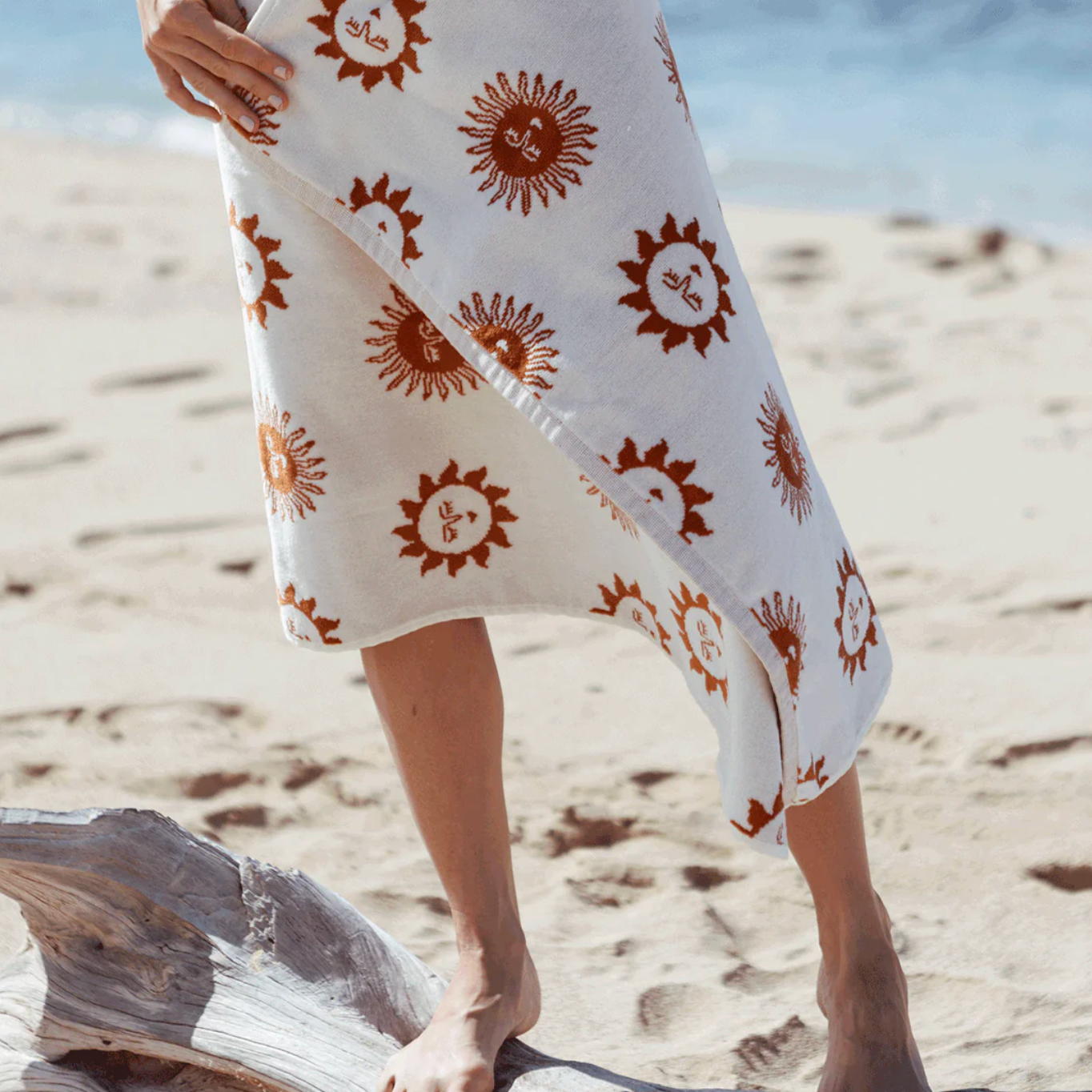 Person holding a white towel with brown sun patterns on a sandy beach.
