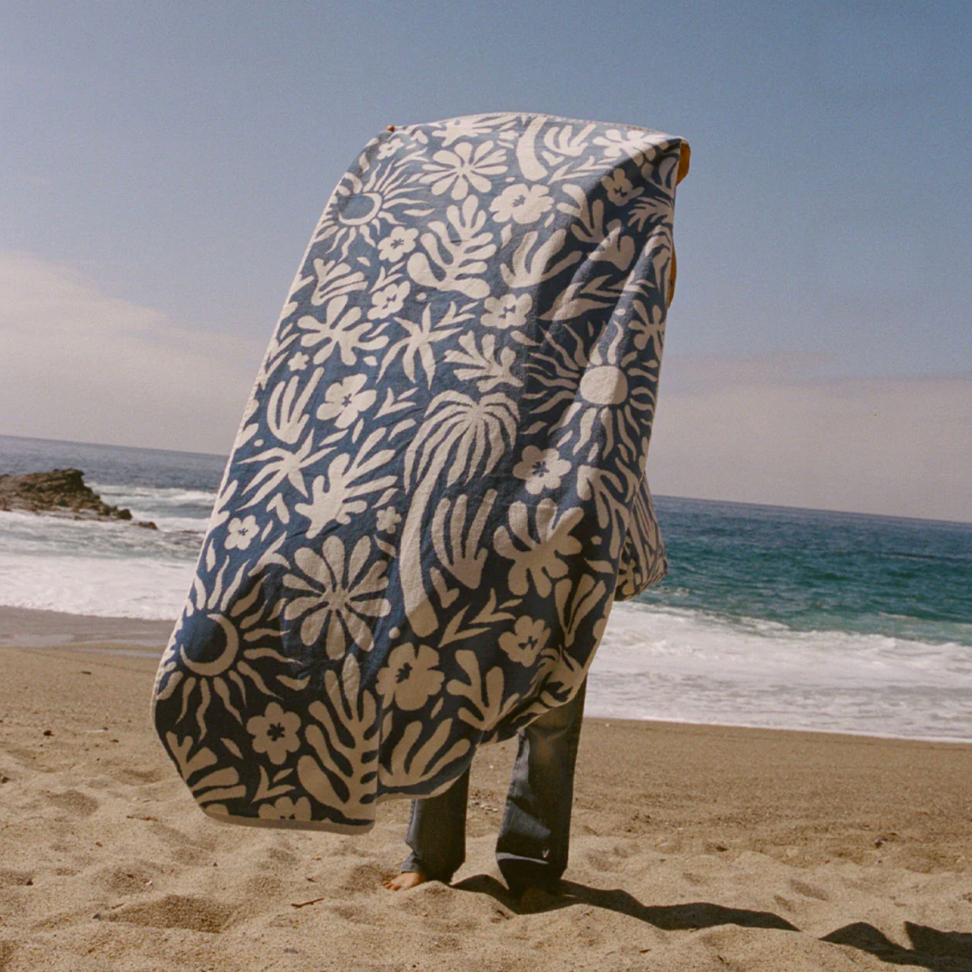 Person holding a floral-patterned towel on a beach